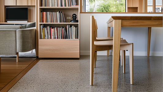 A modern living space featuring a tasmanian oak dining table, minimalist chairs, a bookshelf with records, and a cozy sofa.