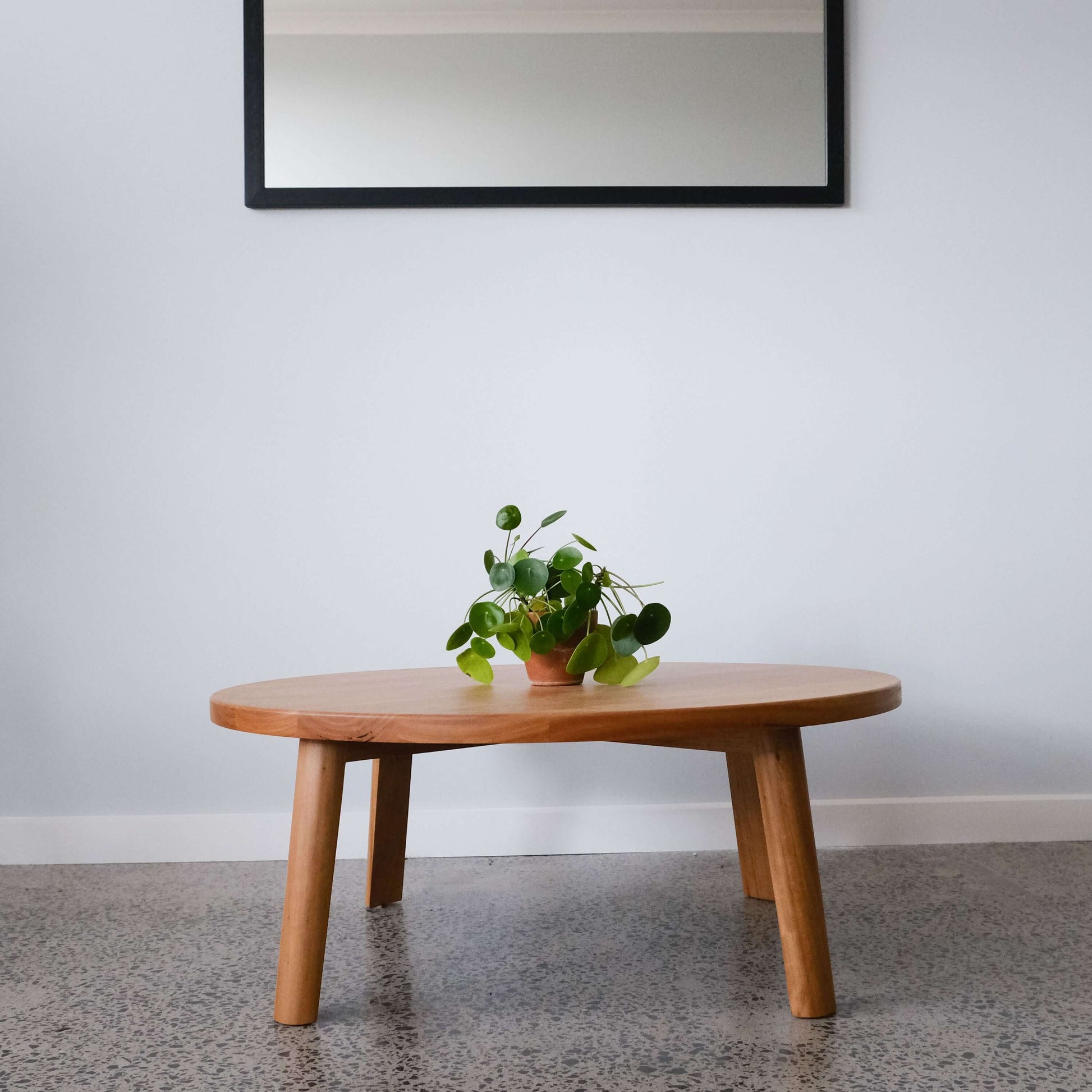 Round timber coffee table with a plant on a gray floor and white wall background