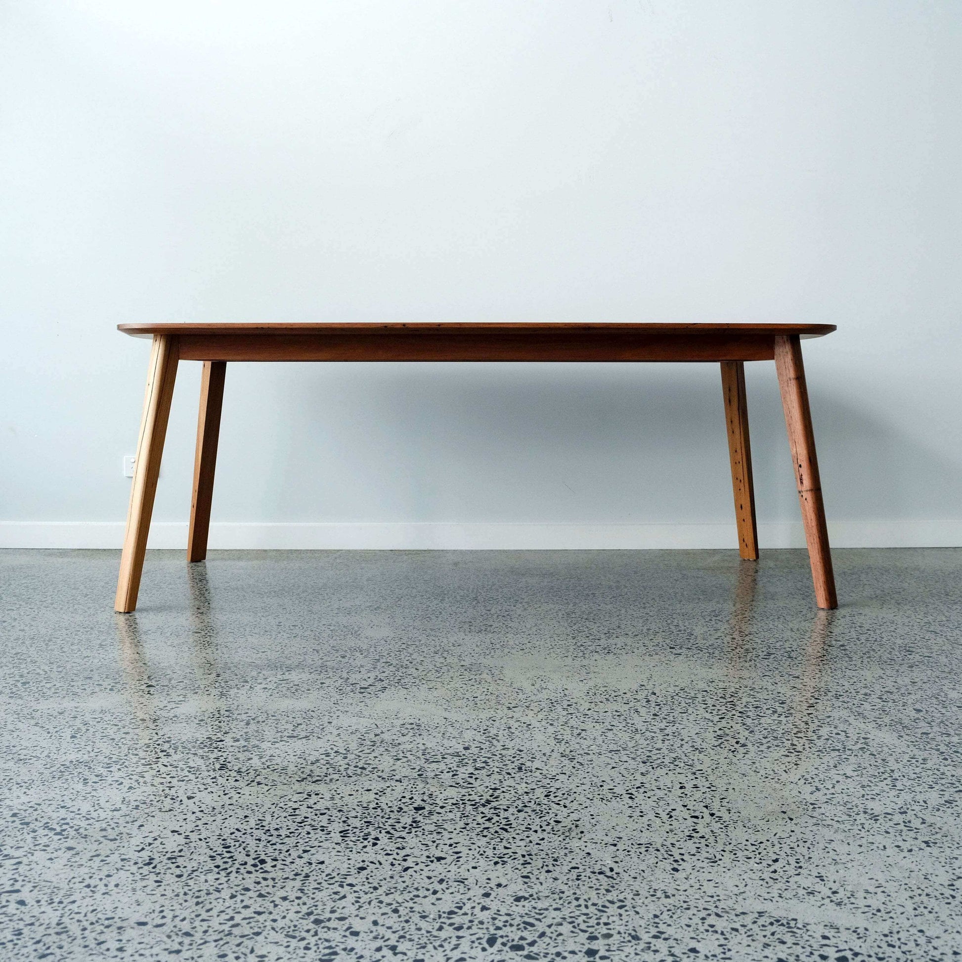 reclaimed timber dining table on a concrete floor with a light gray wall background