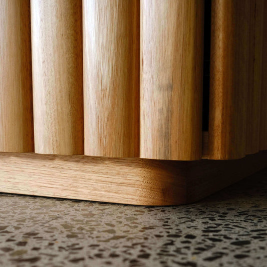 Close-up of a oak cabinet with vertical slats on a textured floor.