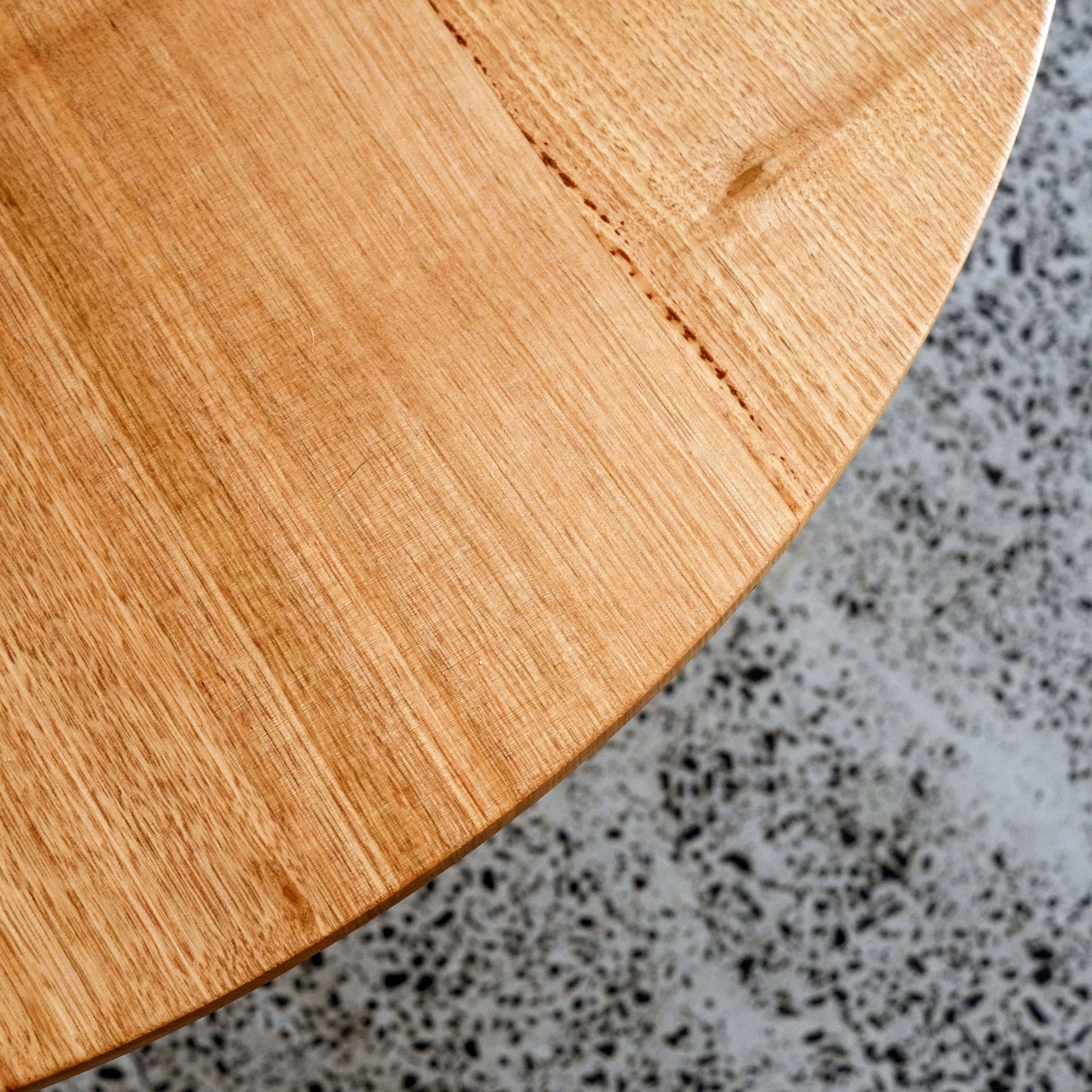 Close-up of a solid timber round dining table top on a speckled gray surface