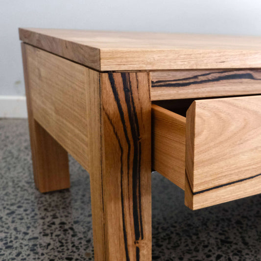 Wooden coffee table with a drawer open on a speckled gray floor.