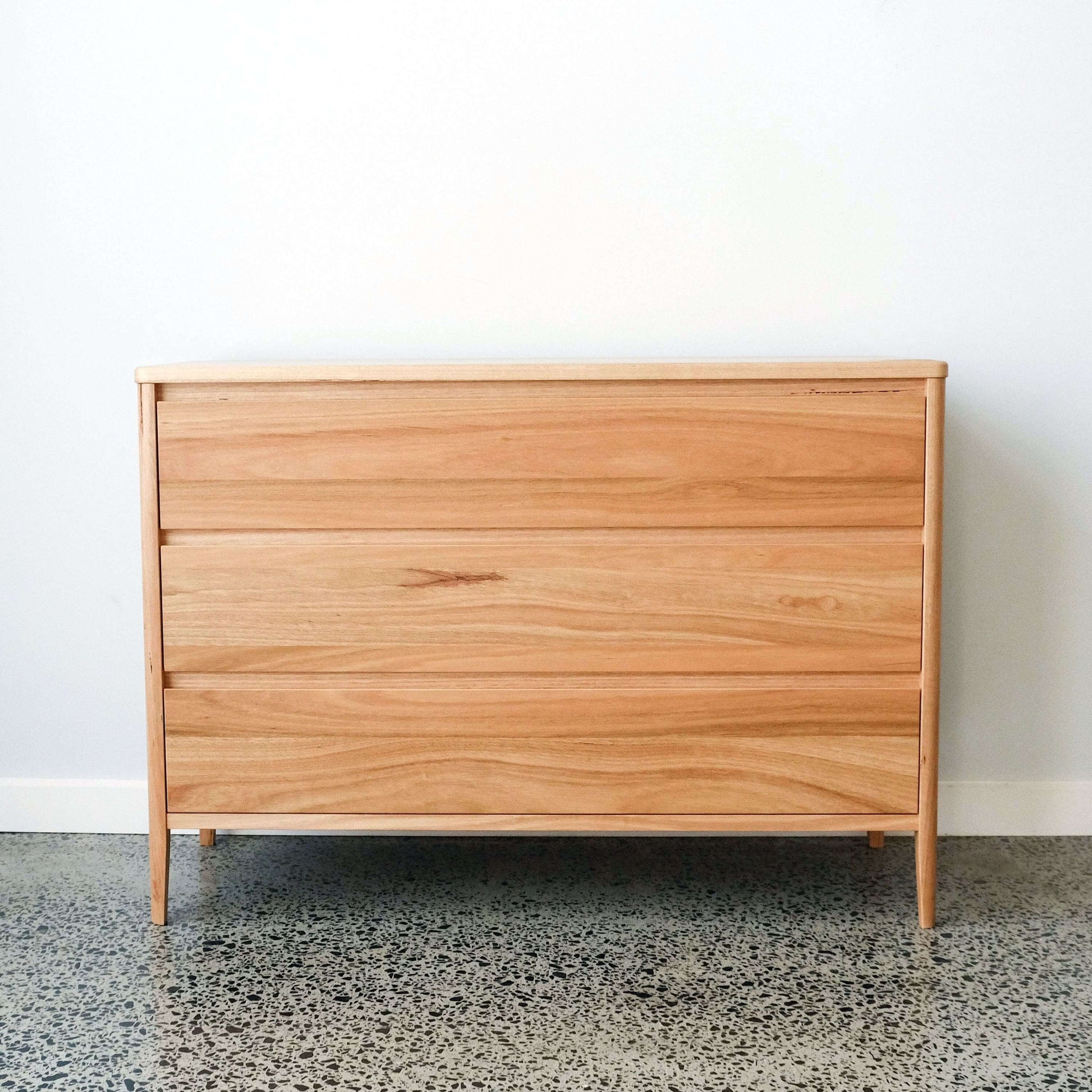 solid timber dresser with three drawers on a concrete floor against a white wall
