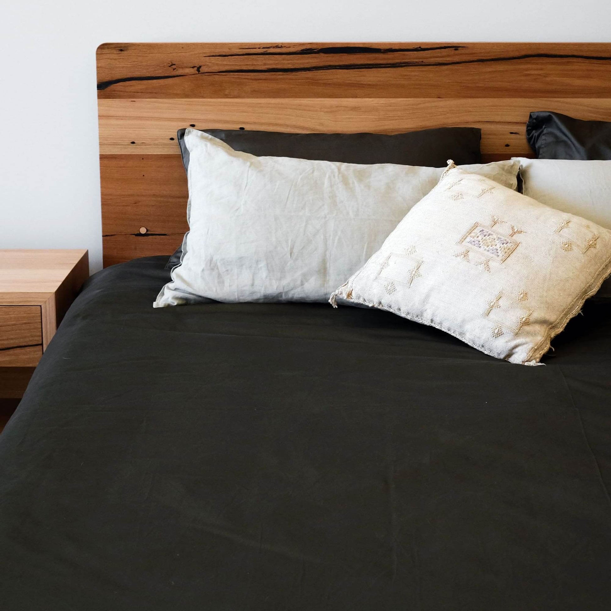 Contemporary Plymouth Panel Timber Bed with recycled timber headboard and stylish cushions on a dark bedding.