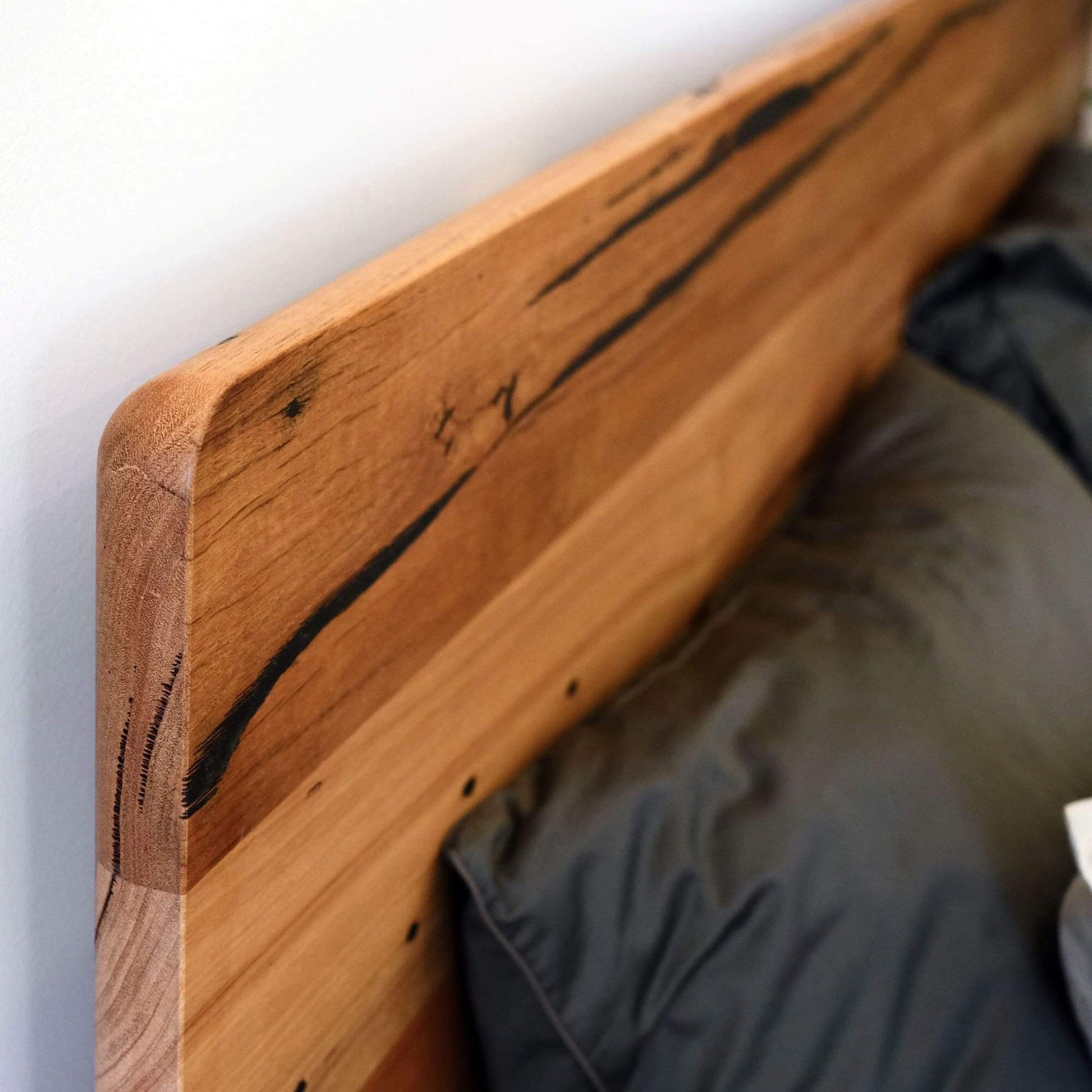 Close-up of the Plymouth Panel Timber Bed headboard made from recycled timber with a sleek curved edge.