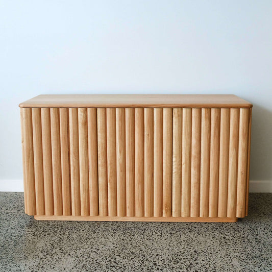 Oak cabinet with slatted design on a speckled floor against a light blue wall